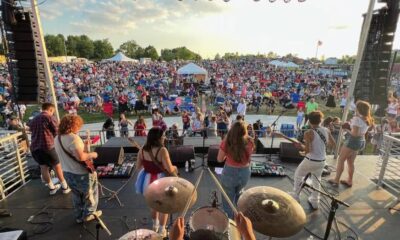Widok z perspektywy sceny na festiwal muzyczny z tłumem ludzi i zespołem na scenie.
